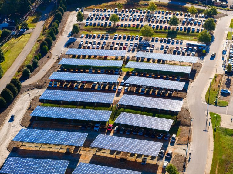 Panele fotowoltaiczne nad parkingiem obok firmy, służąca do wytwarzania energii odnawialnej. Zrównoważona produkcja energii zintegrowana z infrastrukturą miejską.